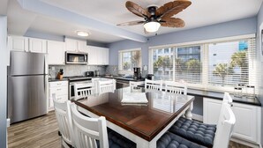A modern kitchen with white cabinetry, a stainless steel refrigerator, a microwave, and a large island with seating. - Seaspray Condos - 210D (Fort Walton Beach)