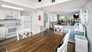 A modern kitchen with white appliances, a wooden dining table, and a cozy seating area with a bed and a chair.
