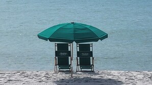Two beach chairs under a green umbrella on a sandy beach with the ocean in the background.