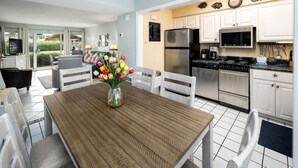 Une cuisine moderne avec des meubles blancs, des appareils en acier inoxydable et un coin repas comprenant une table et des chaises en bois.