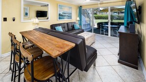 Uma sala de jantar com mesa e cadeiras de madeira, um sofá e uma televisão.