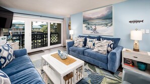 Un salon avec un canapé bleu, une table basse blanche et un tableau représentant une scène de plage.