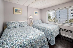 A bedroom with two beds, a window with blinds, and two framed pictures on the wall. - Seaspray Condos - 214C (Fort Walton Beach)