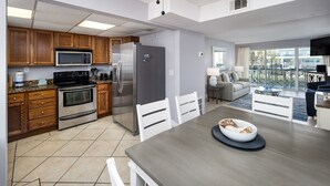 A modern kitchen with stainless steel appliances, wooden cabinets, and a dining area with a large table and chairs. - Seaspray Condos - 214C (Fort Walton Beach)