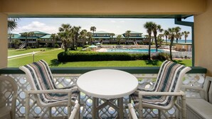 A balcony with wicker furniture, a pool, and a view of a resort building. - Seaspray Condos - 214C (Fort Walton Beach)