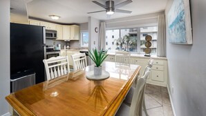 Une cuisine moderne avec une table à manger en bois, des chaises blanches et un réfrigérateur noir.