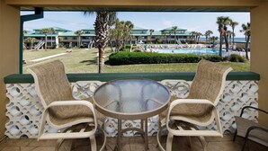 Une terrasse avec deux fauteuils en osier et une table en verre, donnant sur une piscine et les bâtiments du complexe hôtelier.