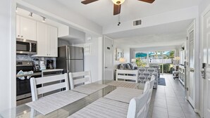 Una cocina moderna con muebles blancos, electrodomésticos de acero inoxidable y un comedor con mesa de vidrio y sillas blancas.