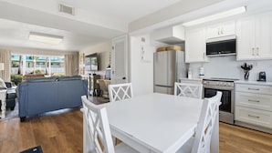A modern kitchen with white cabinetry, a built-in oven, and a dining area with a white table and chairs. - Seaspray Condos - 215B (Fort Walton Beach)