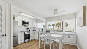 A modern kitchen with white cabinetry, a built-in oven, and a dining area with white chairs and a table. - Seaspray Condos - 215B (Fort Walton Beach)
