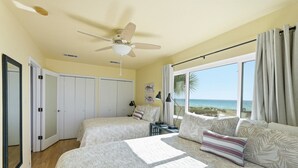 Une chambre avec deux lits, un ventilateur de plafond et une grande fenêtre donnant sur la plage.