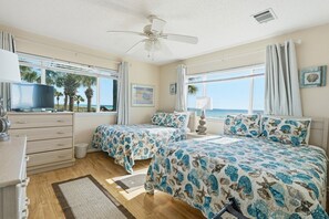Une chambre d’hôtel avec deux lits, une télévision, un ventilateur de plafond et une vue sur la mer.