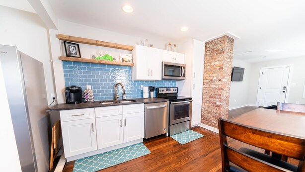 Una cocina moderna con armarios blancos, salpicadero azul y pared de ladrillo decorativa.