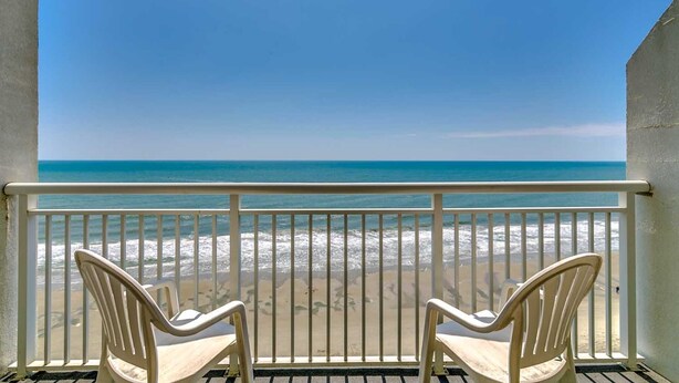A balcony with two white plastic chairs facing a beach with waves and clear blue sky. - · Oceanfront King Jacuzzi Suite - Beautiful Views! (Myrtle Beach)