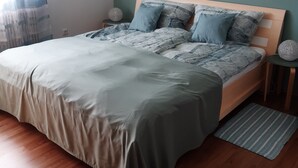 A bedroom with a bed, a bedside table, a lamp, a rug, and a framed picture on the wall.