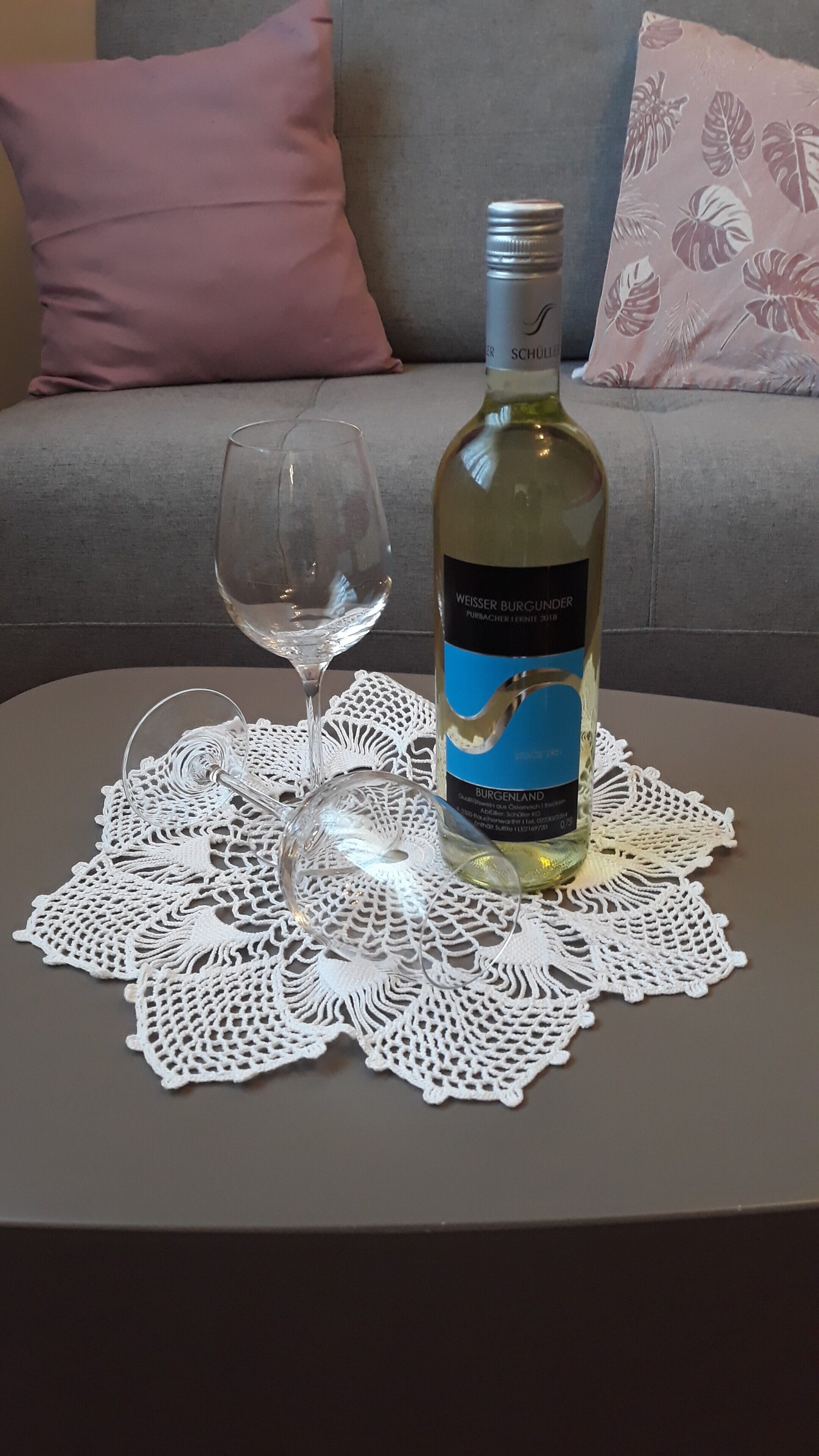 A bottle of Weisser Burgunder wine on a table with a doily, a wine glass, and a couch in the background.