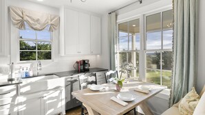 A modern kitchen with white cabinetry, a wooden dining table, and a view of the garden through large windows. - Unique hilltop home with amazing views and close to Main Street; with Pickleball (Fredericksburg)