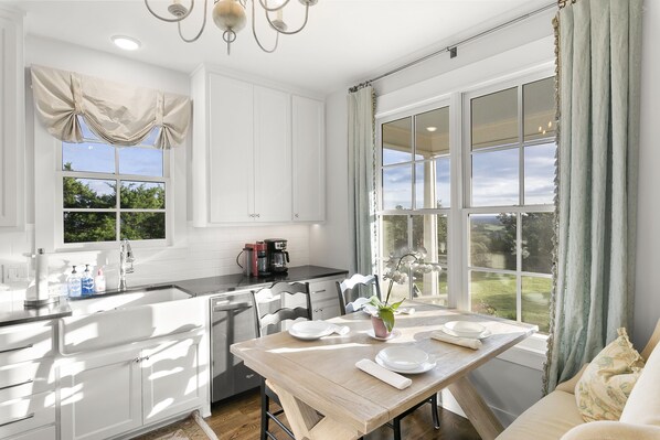 Una cocina moderna con armarios blancos, una mesa de comedor de madera y vistas al jardín a través de amplios ventanales.