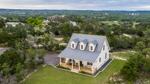 A two-story house with a covered porch, a metal roof, and a view of the surrounding landscape. - Unique hilltop home with amazing views and close to Main Street; with Pickleball (Fredericksburg)