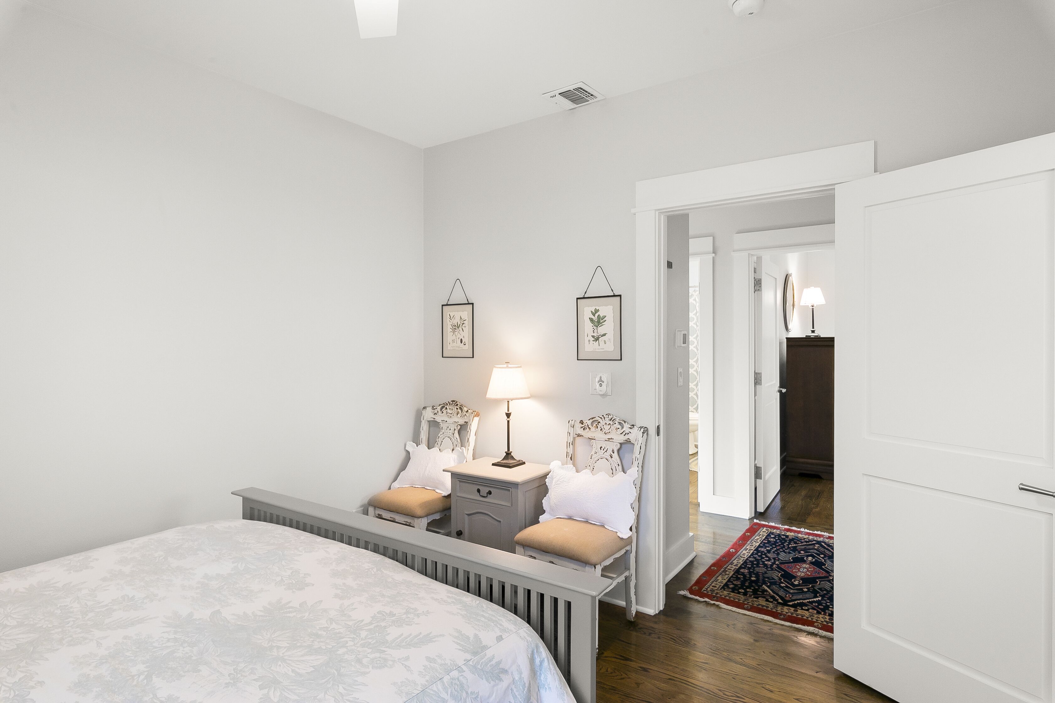 A bedroom with a bed, bedside tables, a lamp, and two chairs.