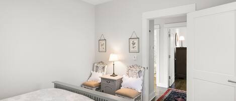 A bedroom with a bed, bedside tables, a lamp, and two chairs.