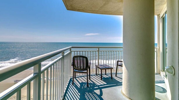 A balcony with a view of the ocean, a chair, a small table, and a concrete pillar. - · Beautiful Oceanfront Deluxe - Pool, Lazy River, Hot Tub and more! (Myrtle Beach)