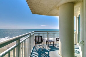 A balcony with a view of the ocean, a chair, a small table, and a concrete pillar. - · Beautiful Oceanfront Deluxe - Pool, Lazy River, Hot Tub and more! (Myrtle Beach)
