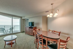 A hotel room with a balcony, a dining table with chairs, a TV, and a chandelier. - · Beautiful Oceanfront Deluxe - Pool, Lazy River, Hot Tub and more! (Myrtle Beach)