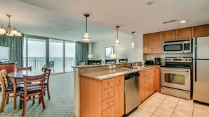 A modern kitchen with wooden cabinets, stainless steel appliances, and a dining area with a table and chairs. - · Luxury Oceanfront 2Bdrm Condo - Free Wifi, Pool, Hot Tub, Lazy River! (Myrtle Beach)