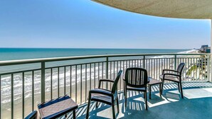 A balcony with a view of the beach and ocean. There are three chairs and a small table. - · Luxury Oceanfront 2Bdrm Condo - Free Wifi, Pool, Hot Tub, Lazy River! (Myrtle Beach)