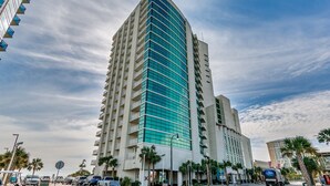 Un grand hôtel moderne à la façade incurvée, doté de nombreux balcons et d’un parking où se trouvent des voitures et un véhicule de golf.