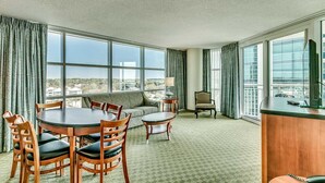 Une chambre d’hôtel dotée d’une grande fenêtre, d’une table à manger avec des chaises, d’un canapé, d’une petite table d’appoint et d’un bureau avec un ordinateur.