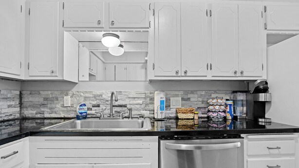 A kitchen with white cabinets, a stainless steel dishwasher, a granite countertop, and a backsplash with gray tiles.