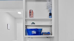 A room with a white wall, a blue-framed shelf unit, a black chair, and a blue storage bin.