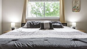 A neatly made bed with a patterned bedspread, two bedside lamps, and a window with curtains.