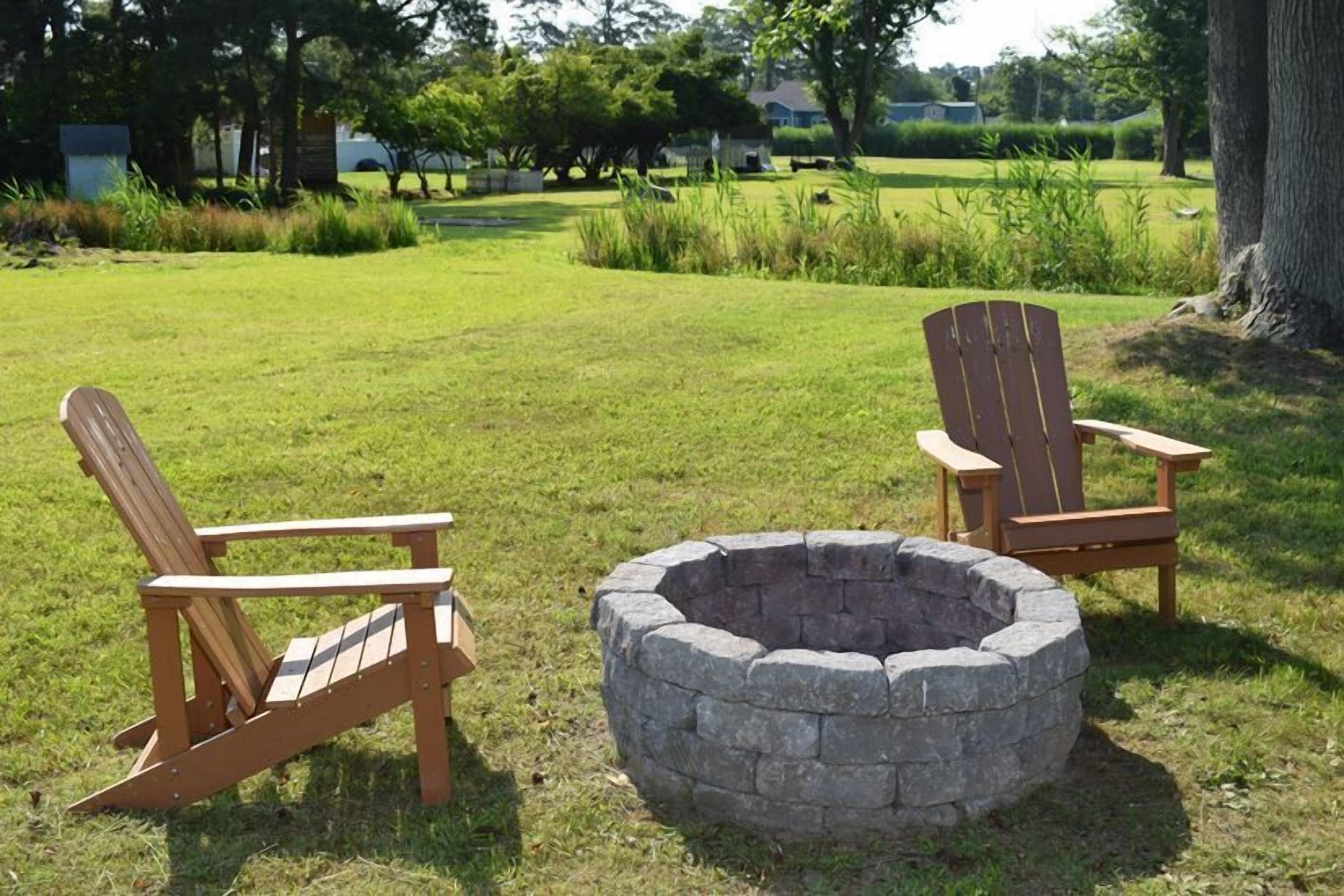 Deux fauteuils Adirondack et un foyer en pierre, le tout installé dans un espace extérieur verdoyant.