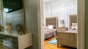 A bedroom with a bed, bedside tables, a TV mounted on the wall, and a wooden floor. - Luxury Home away from Home (Georgetown)