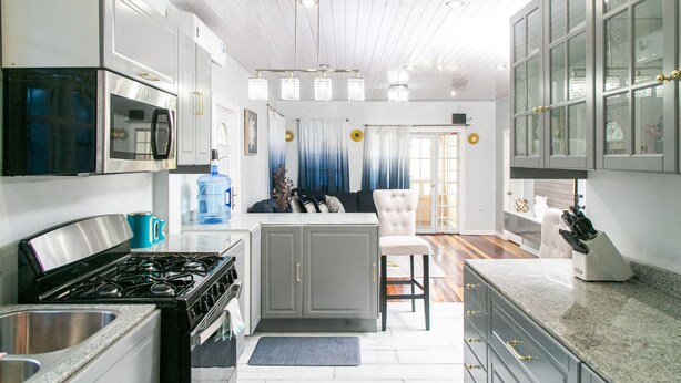 A modern kitchen with a stove, microwave, and cabinets. There is a bar stool and a water dispenser. - Luxury Home away from Home (Georgetown)