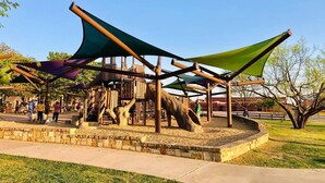 A playground with a wooden structure and shaded areas. - •The Book Nook• Books•Arcade•Grill•Workspace! (North Richland Hills)