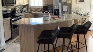 Una cucina moderna con isola centrale, sgabelli da bar, microonde, piano cottura, frigorifero e lampade a sospensione.