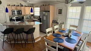 Una cucina moderna con isola centrale, sgabelli da bar, un tavolo da pranzo con sottopiatti e una ventola a soffitto.
