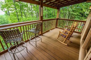 A wooden deck with two wicker chairs and a rocking chair, surrounded by a wooden railing, overlooking a forested area. - Breathtaking MtnCity View/HotTub/5min->PForge Pkwy (Sevierville)