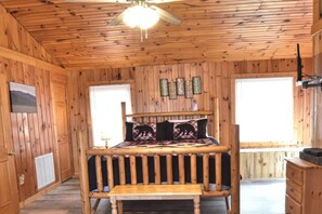 Une chambre dans une cabane en bois, avec un lit, un ventilateur de plafond et une fenêtre.