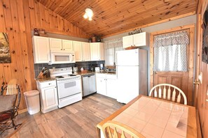 A compact kitchen with white cabinets, a microwave, a stove, and a refrigerator. There is a wooden dining table with chairs. - Breathtaking MtnCity View/HotTub/5min->PForge Pkwy (Sevierville)