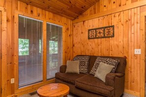 A wooden interior with a brown sofa, patterned cushions, and a round wooden table.