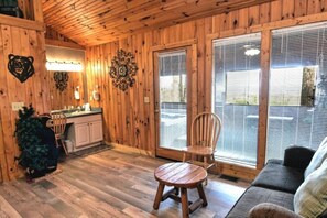 A cozy cabin interior with wooden walls, a dining area with a table and chairs, a kitchen with a sink and cabinets, and large windows with blinds. - Breathtaking MtnCity View/HotTub/5min->PForge Pkwy (Sevierville)