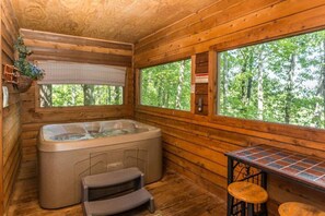 A wooden cabin interior with a hot tub, a small step stool, and a bar area with stools. - Breathtaking MtnCity View/HotTub/5min->PForge Pkwy (Sevierville)