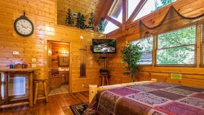 Acogedora habitación de cabaña de madera con cama, televisor, reloj y chimenea.