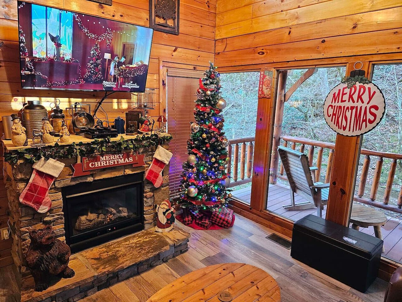 A cozy cabin interior with a fireplace, a Christmas tree, and a television mounted on the wall.