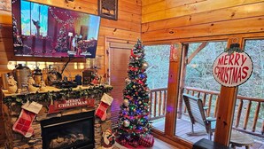 Interior acogedor de una cabaña con chimenea, un árbol de Navidad y un televisor montado en la pared.